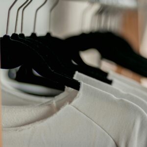 Close-up of white t-shirts hanging neatly on black hangers in a minimalist indoor closet setting.